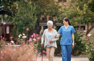 Younger nurse walking outdoors with older resident