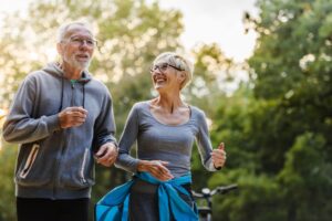 Two older adults in workout clothing smiling and going for jog outdoors