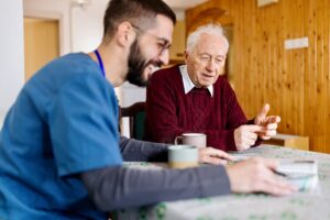 Caretaker and man sitting at table and drinking coffee and reading newspaper