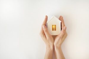 A woman’s hands holding a wood model of a home with a glowing light inside
