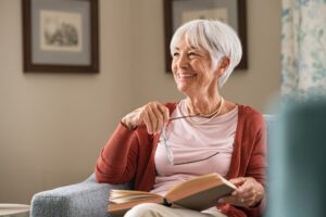 Smiling senior woman sitting on a couch holding a book and eyeglasses