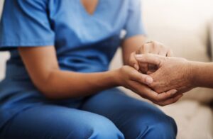 Close-up of a caregiver in blue scrubs holding an elderly person’s hand.  